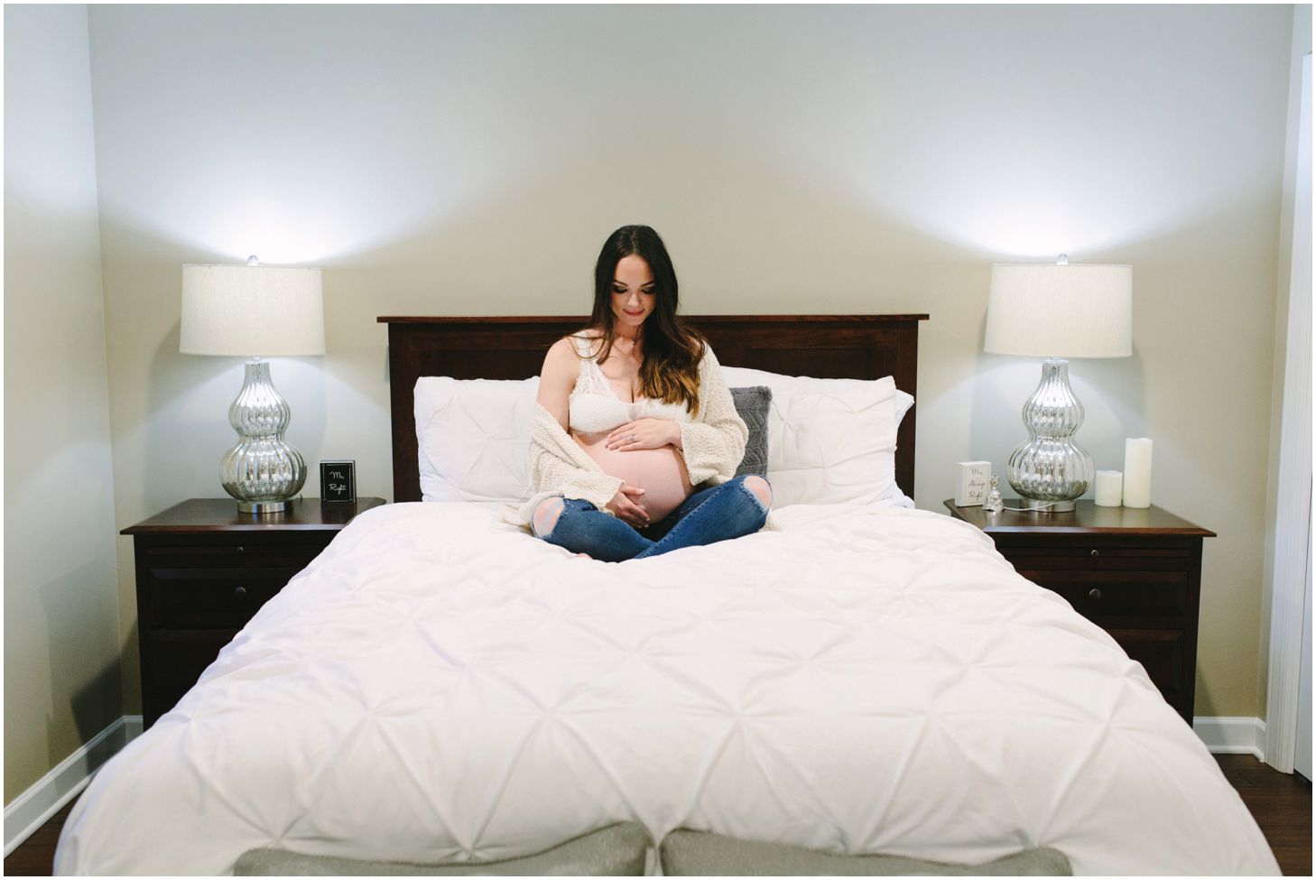 mom holds her belly, sitting on a white bed | maternity session