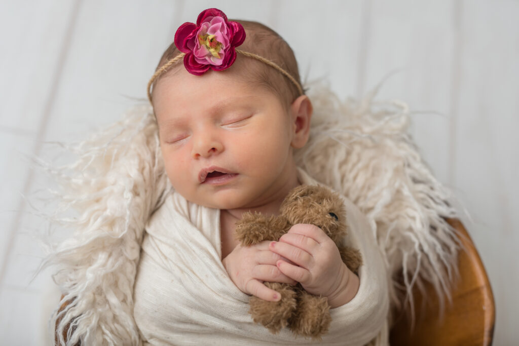 Newborn baby girl holding teddy bear at a vintage cream-colored photo session at Kelly Adrienne Photography studio