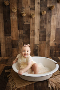 baby sitting and smiling in a white bowl on a wooden backdrop