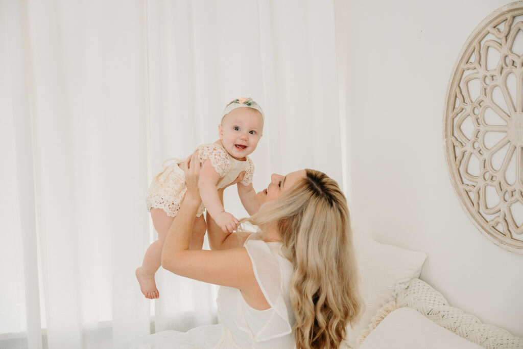 mom holding up six month old baby, cream dress, sitter session