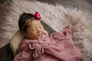 newborn baby girl with pink flower wrap on fur