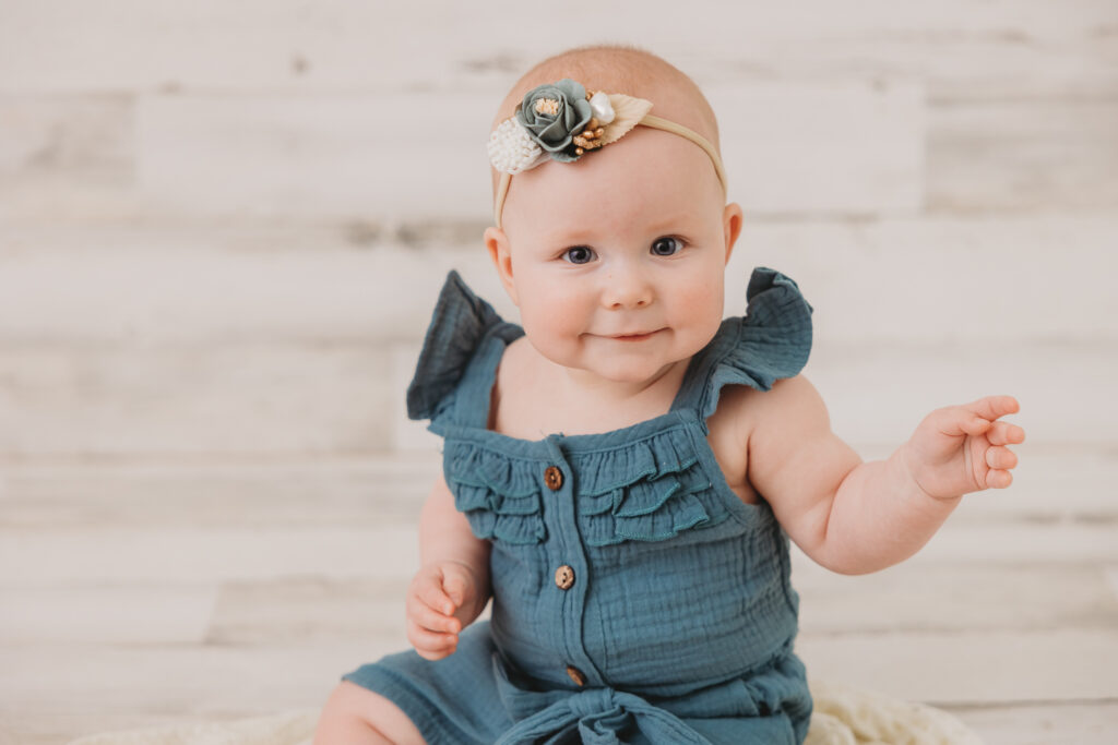 baby in blue romper with headband on white background, sitter session