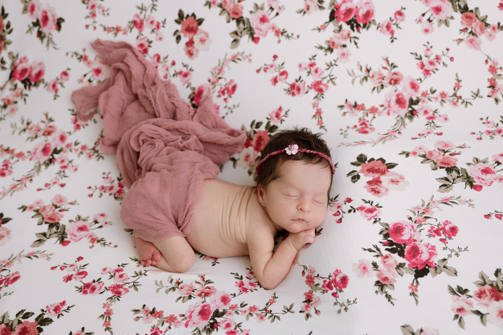 newborn baby girl with pink wrap sleeping on flowered backdrop
