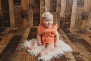 6 month old baby in peach outfit sitting on a fur rug