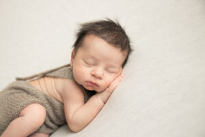 newborn baby boy sleeping on an oatmeal blanket wearing a knit romper