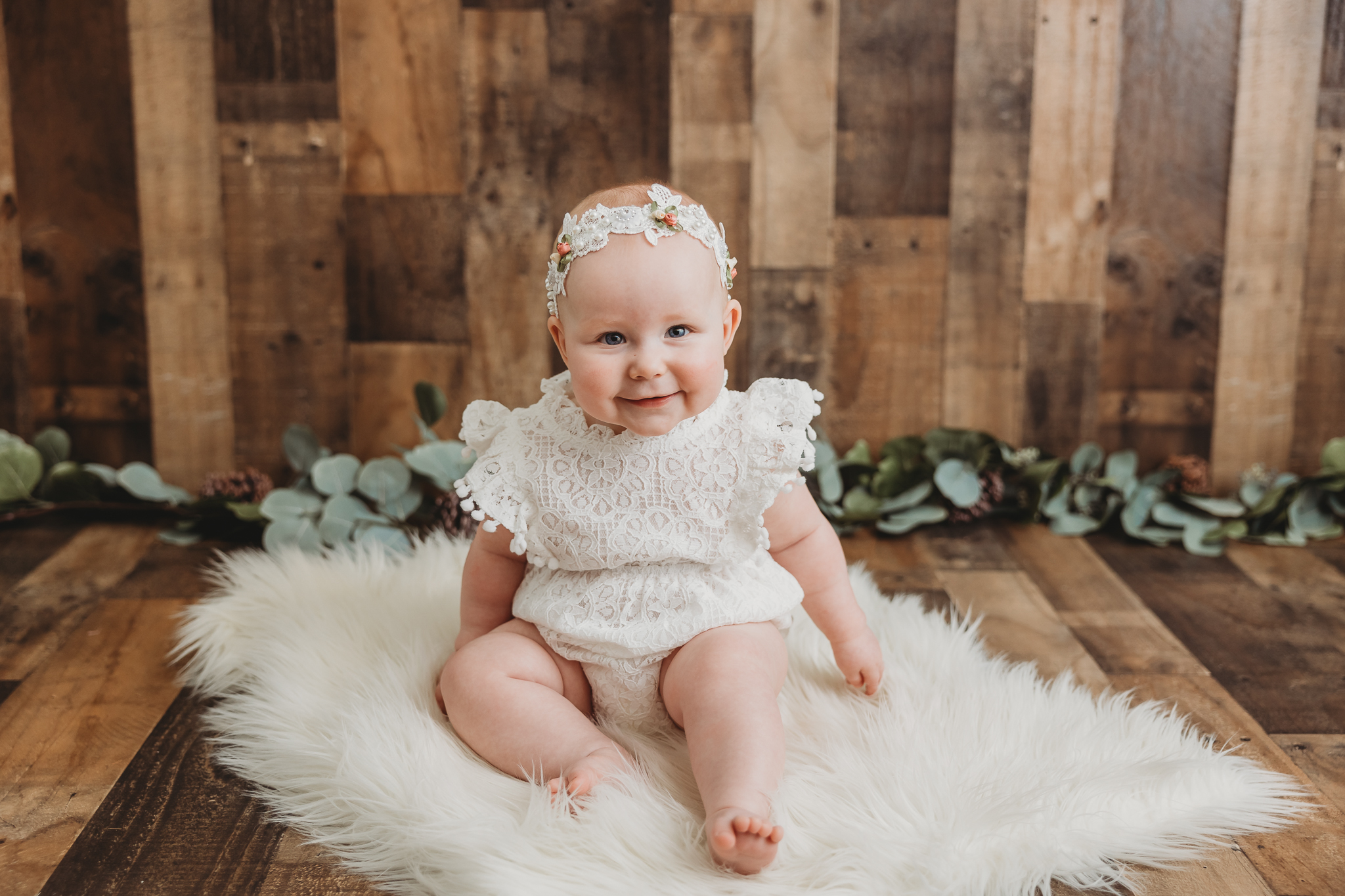 smiling baby sitting on fur with greens and a wooden background, sitter session