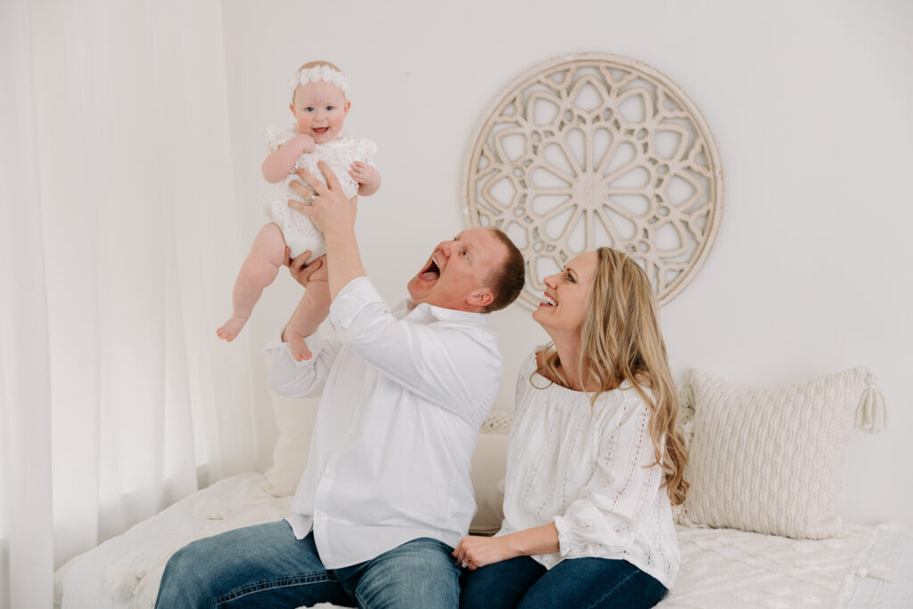 parents sitting on bed holding baby up, boho sitter session