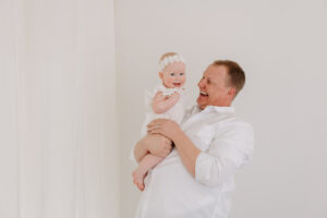 dad laughing with baby girl wearing white, sitter session