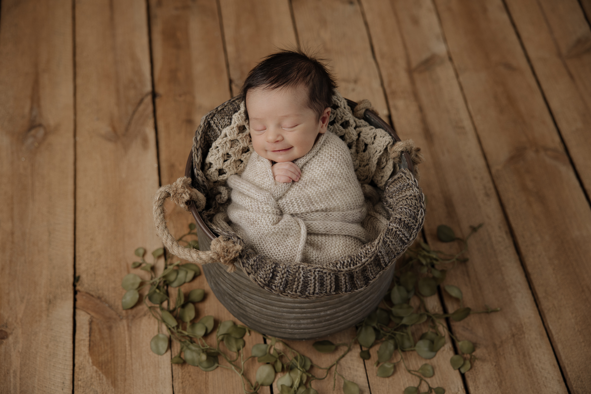 newborn baby boy smiling while wrapped in a blanket on a wooden backdrop
