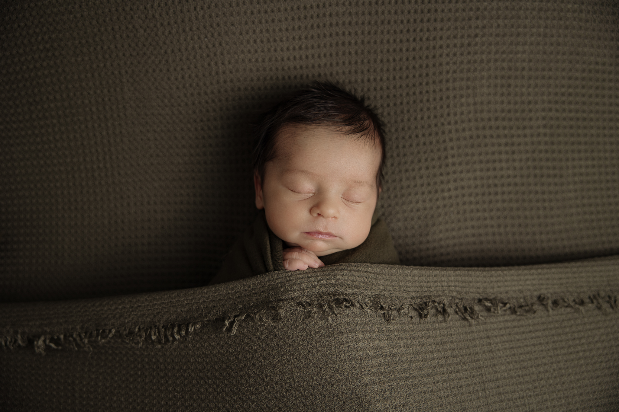 newborn baby boy sleeping while tucked into an olive blanket