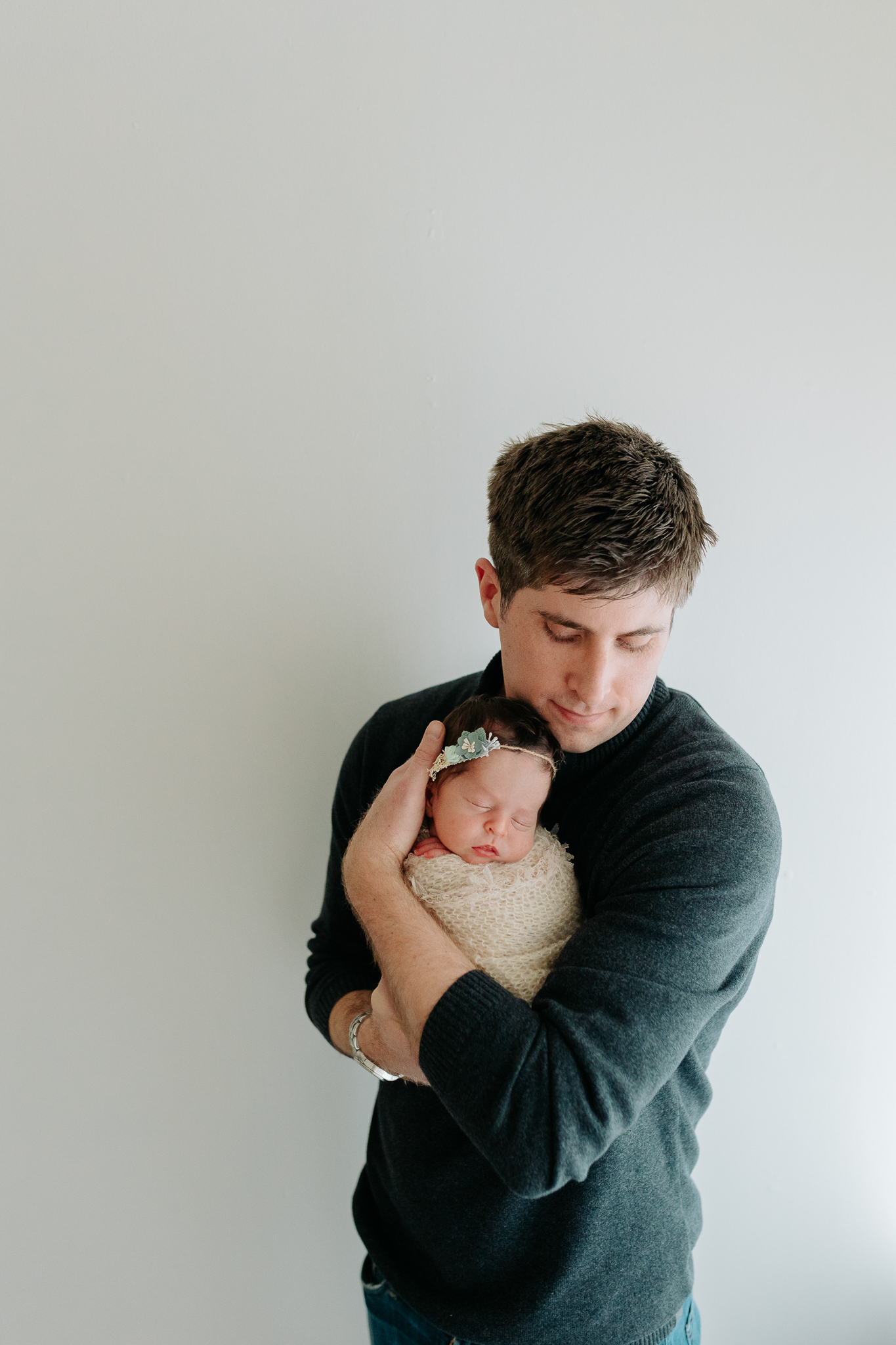 dad snuggling his newborn baby girl with a white wall