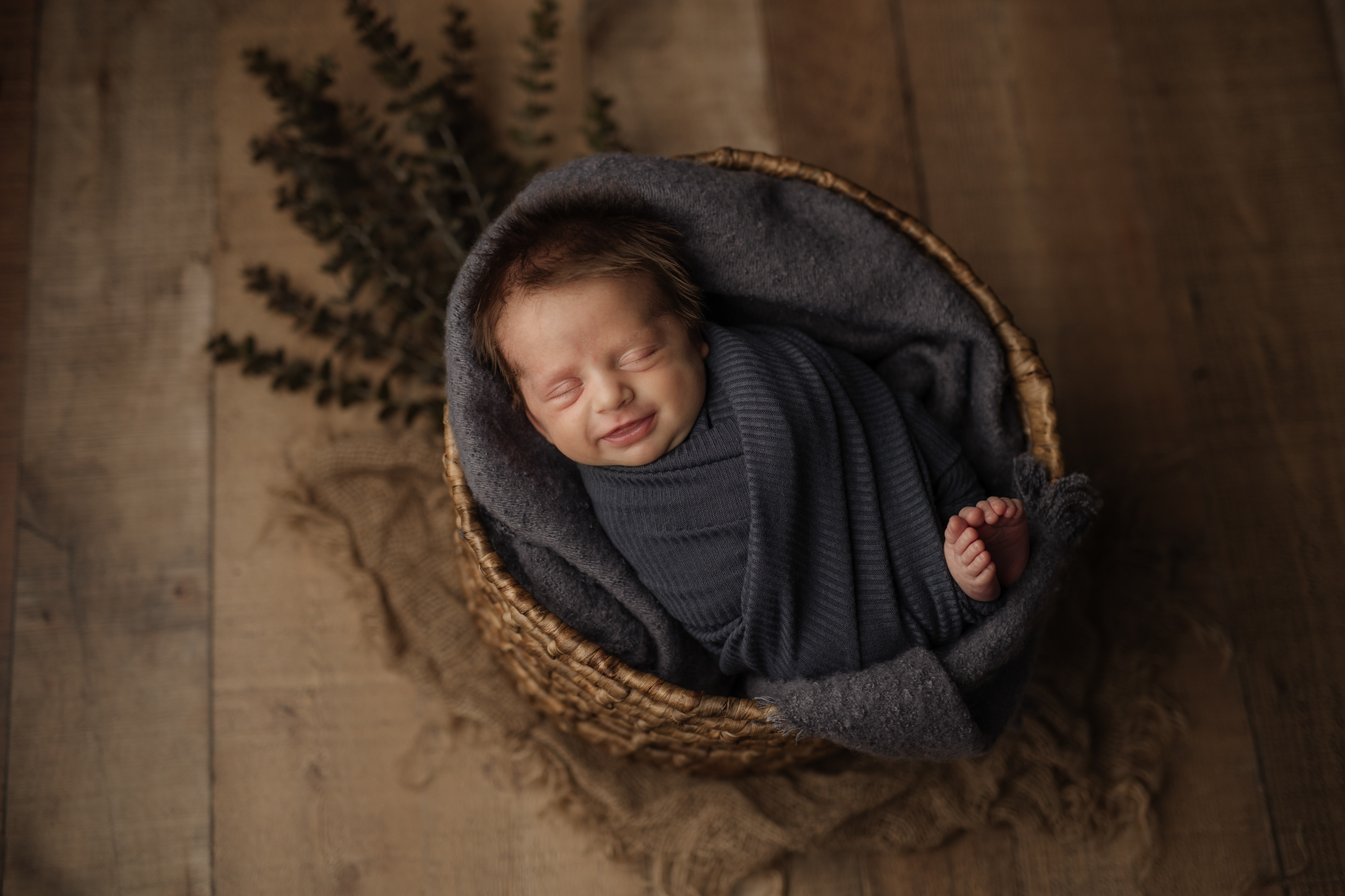 Adorable dark-haired baby boy in a slate blue wrap in a basket, captured by Kelly Adrienne Photography