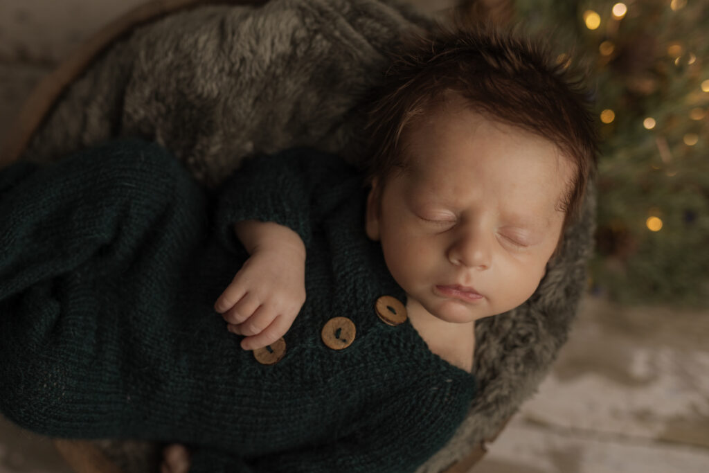 Sweet newborn boy in dark green jammies on a green fur at Kelly Adrienne Photography studio
