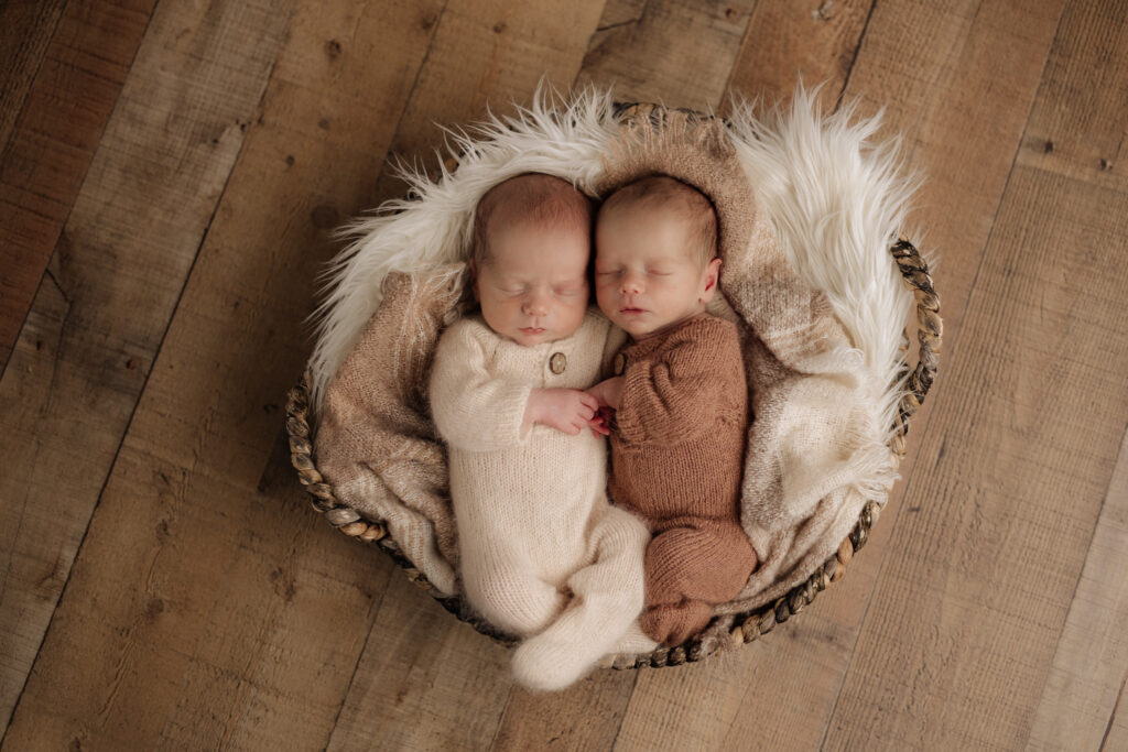 twin newborn boys in neutral pajamas sleeping on white fur