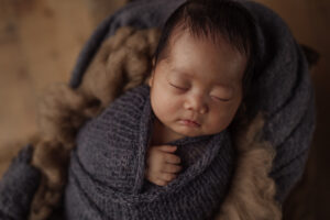 sleeping newborn baby boy wrapped in gray/blue with rustic wood floors