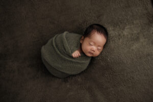 sweet wrapped newborn baby boy sleeping on an olive green blanket