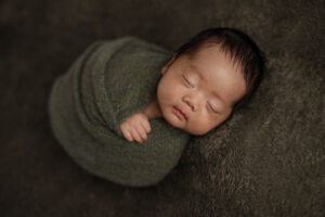 sweet wrapped newborn baby boy sleeping on an olive green blanket