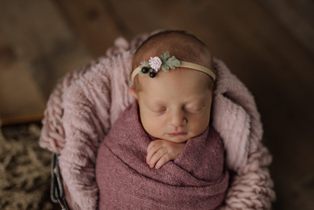 sleeping newborn baby wrapped in a pink blanket with a headband
