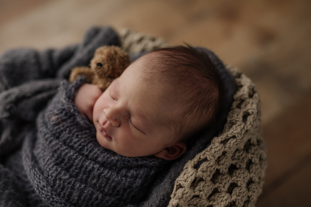 newborn baby boy sleeping on an antique blanket holding a teddy bear