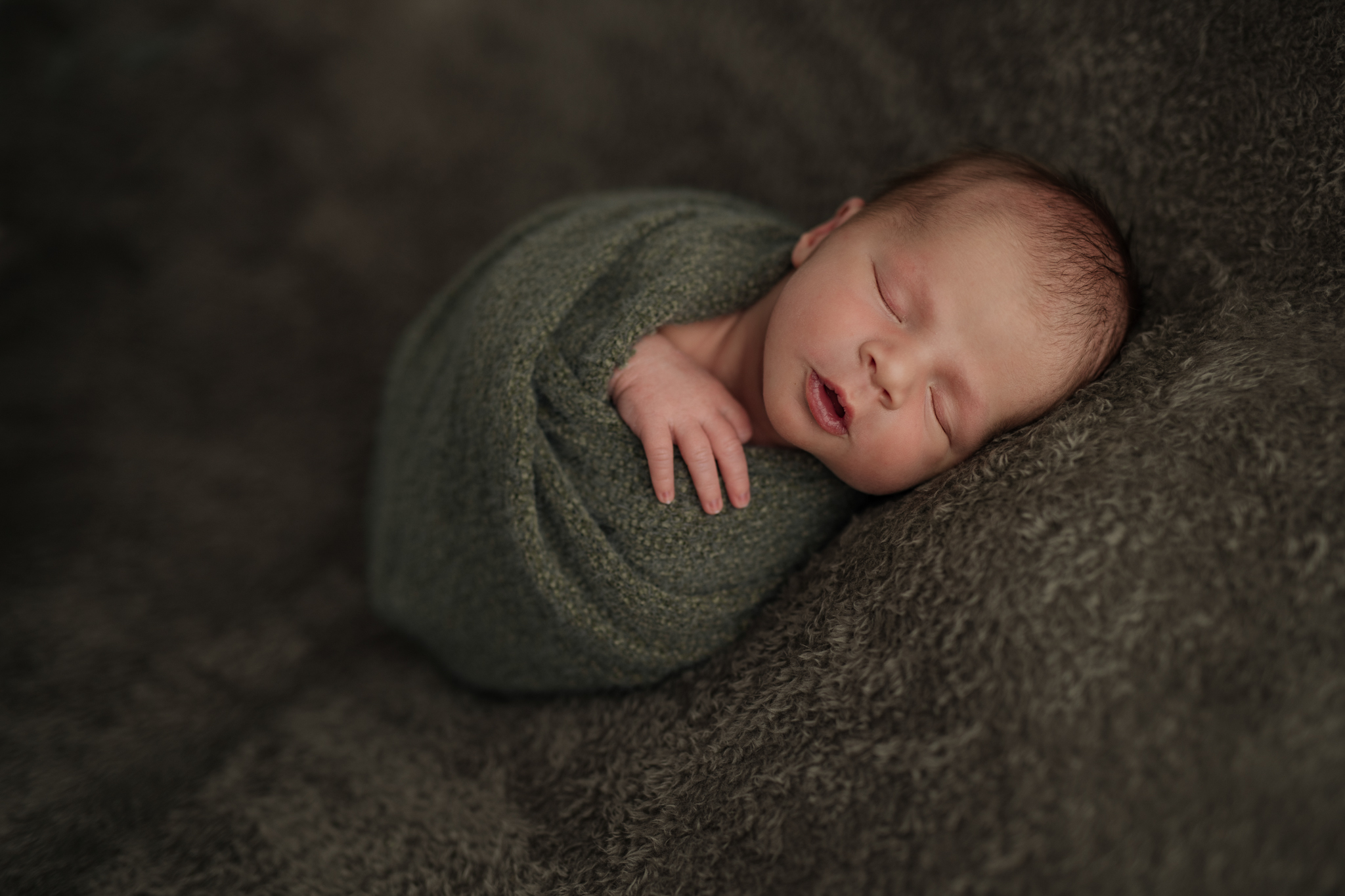 newborn baby boy wrapped in sage green sleeping on a green blanket