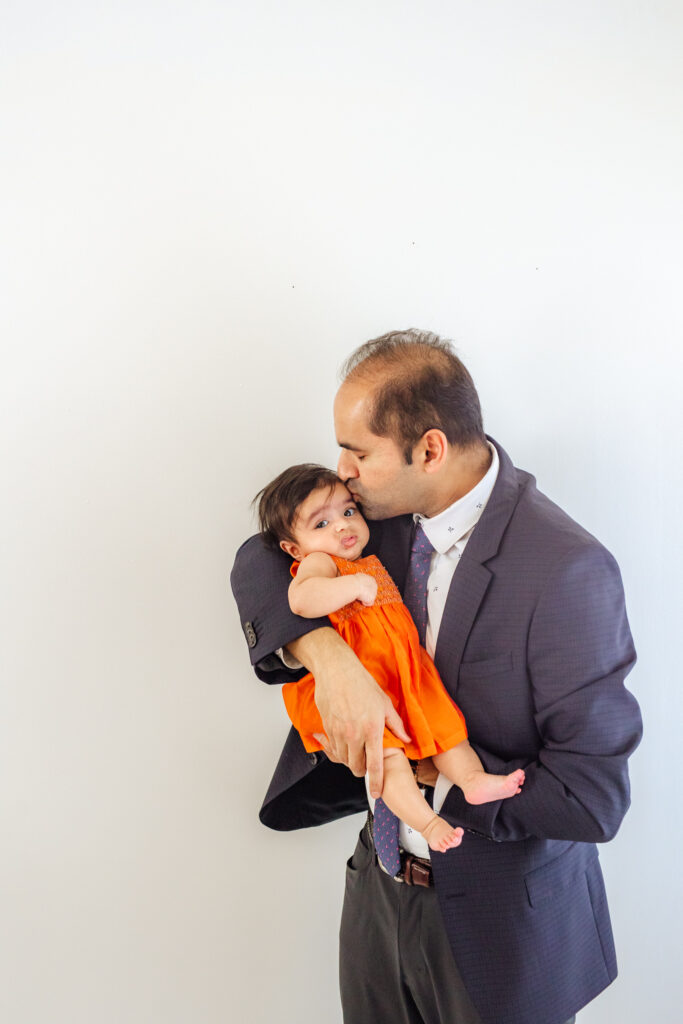 dad kissing 3 month old baby girl in front of a white wall