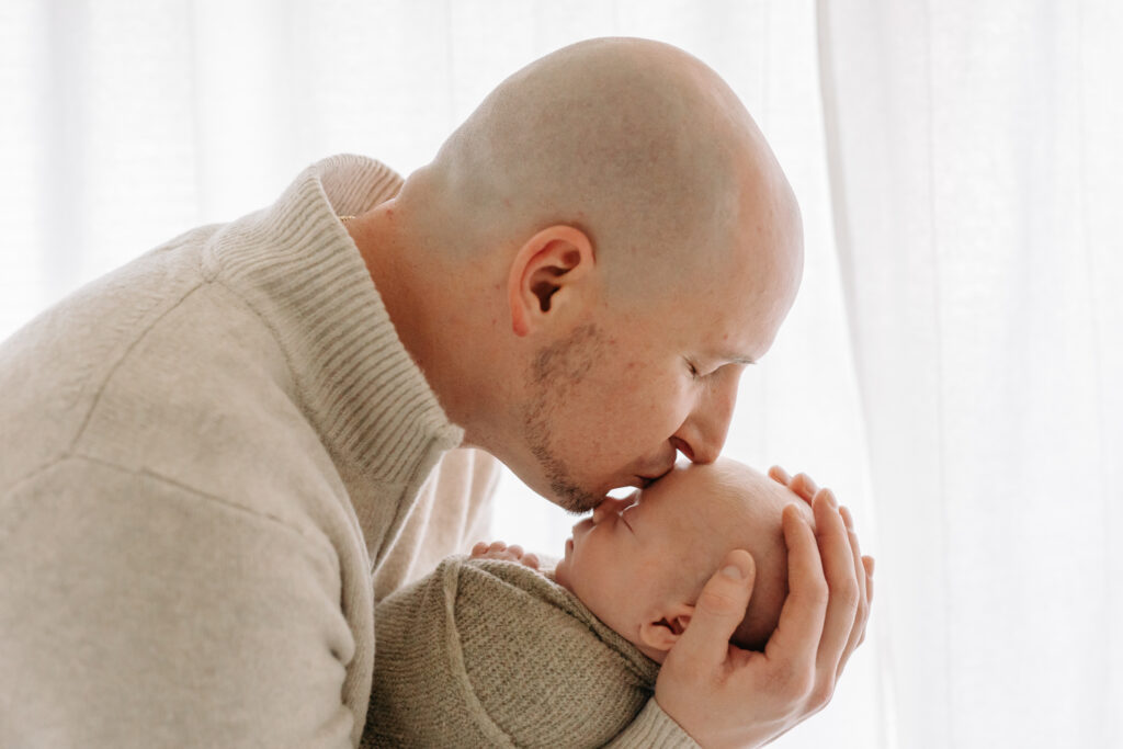 dad kisses his newborn baby against a white background