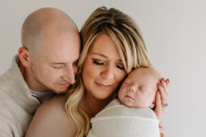mom and dad snuggle with newborn baby with a white background