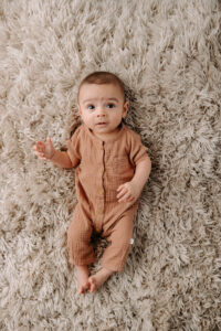 sweet baby boy lying on tan rug in a neutral romper
