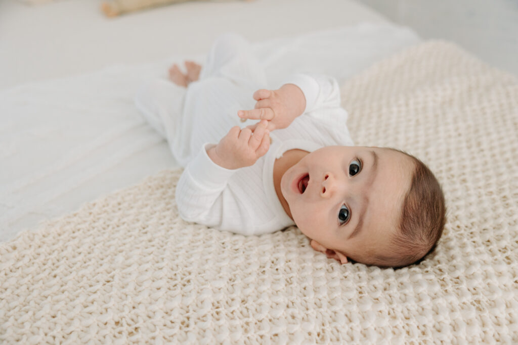 3-month old boy smiling and lying on bed in all white studio