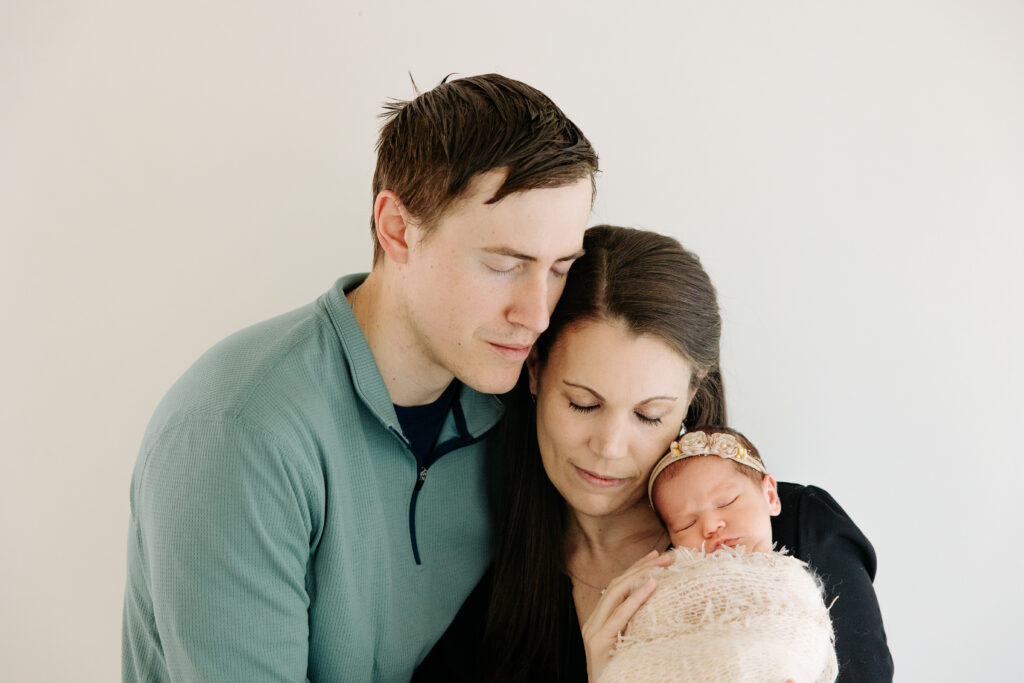 mom and dad snuggle their newborn baby girl with a white background
