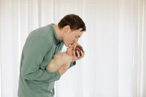 dad kissing his newborn baby girl in front of a window