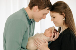 mom and dad holding their newborn baby girl in front of a window