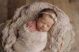 sweet baby girl swaddled in a cream wrap holding a stuffed pink heart