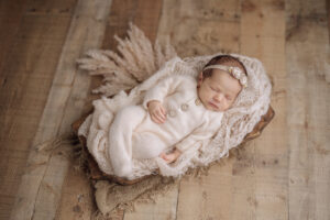 newborn baby girl in cream pajamas sleeping in a basket