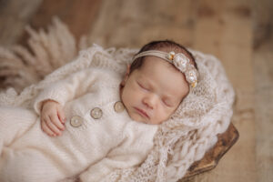newborn baby girl in cream pajamas sleeping in a basket