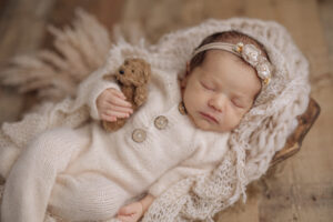 newborn baby girl in cream pajamas holding a teddy bear