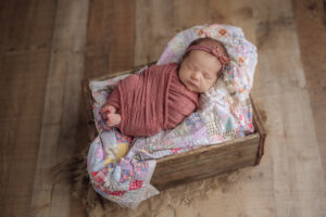 sweet sleeping newborn swaddled in pink lying on an antique quilt