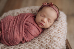 sweet sleeping newborn swaddled in pink with a matching headband