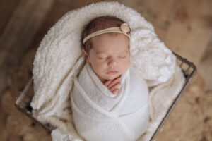 newborn baby girl wrapped in white lying in an antique crate
