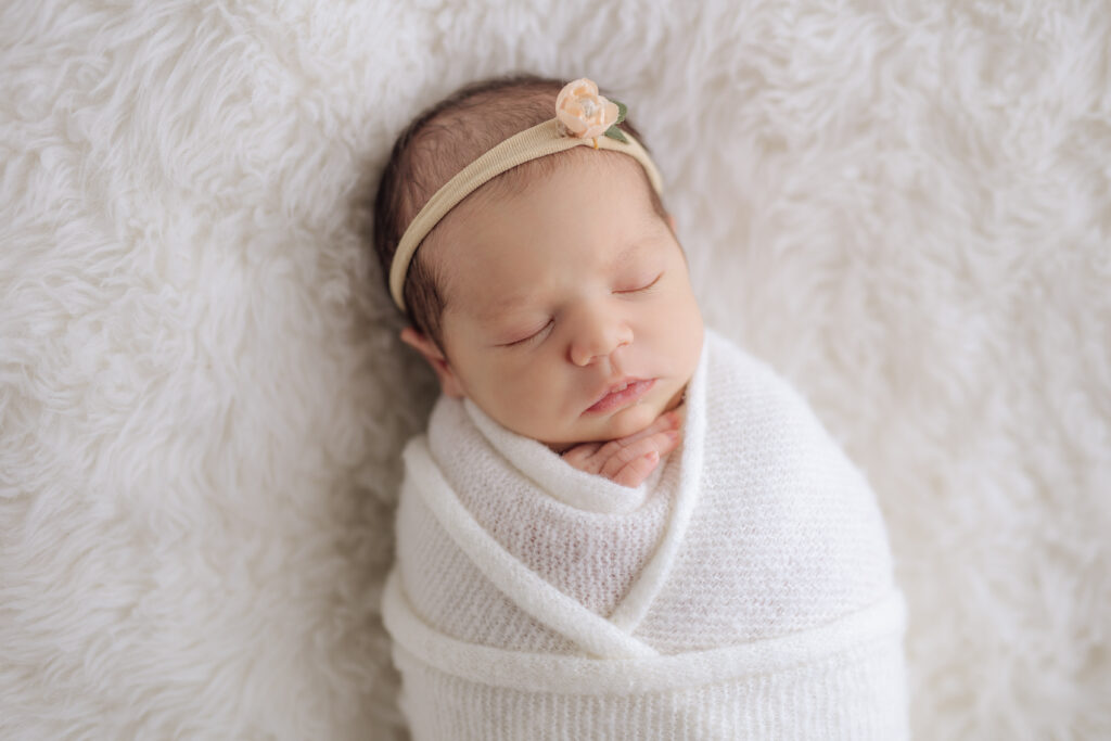 newborn baby girl sleeping on white fur with a white wrap and headband