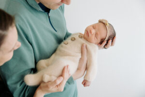sleepy newborn in dad's hands wears cream pajamas and a matching headband