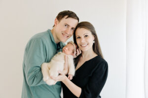 mom and dad snuggle their newborn baby girl with a white background