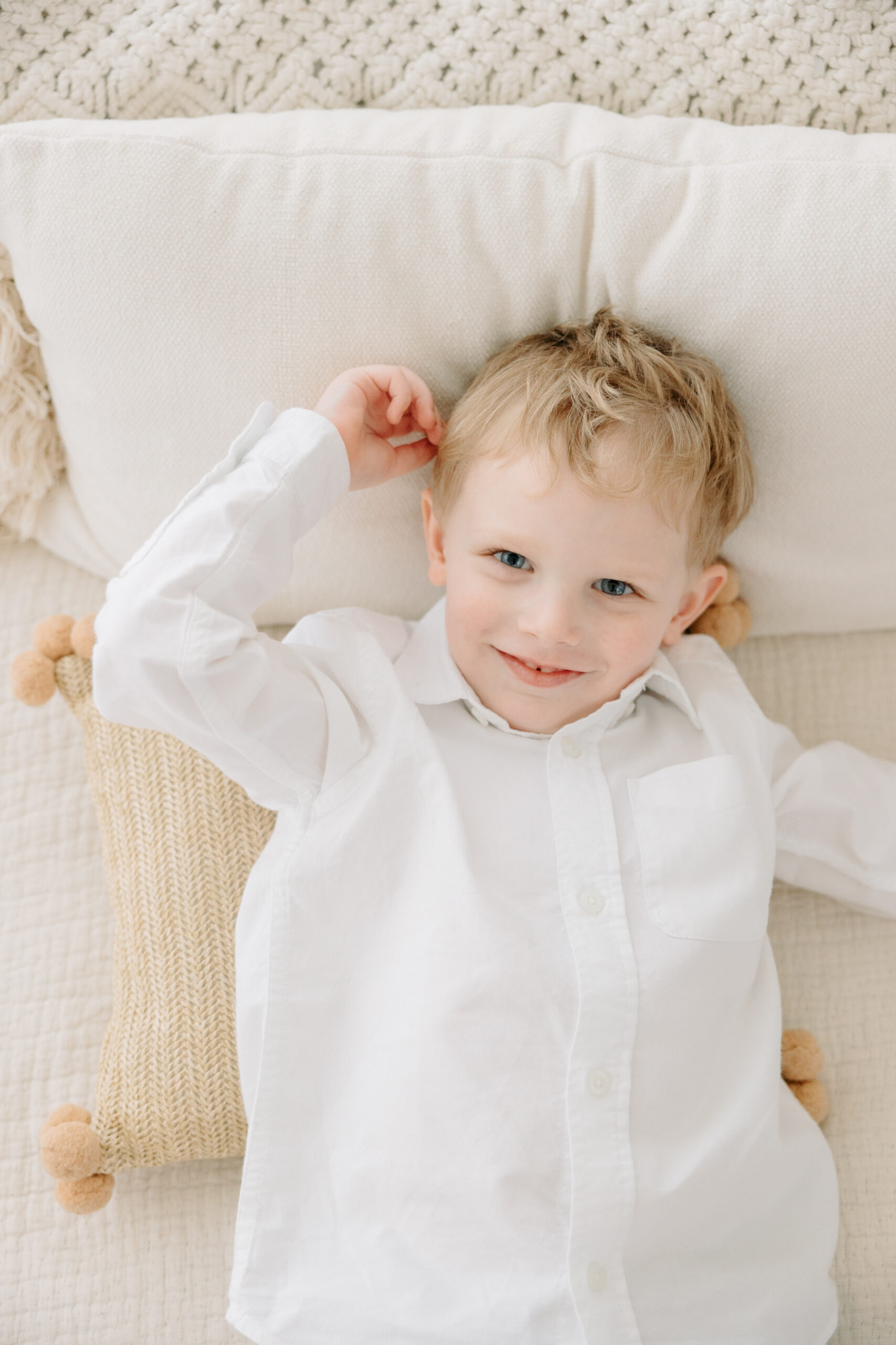 Newborn session with toddler | toddler boy poses on a white bed and smiles at the camera