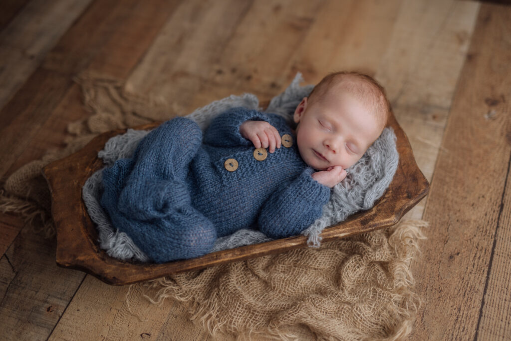newborn baby boy sleeps in a blue pajamas on a rustic wooden floor