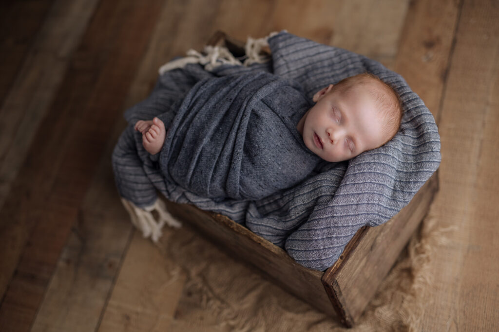 baby boy wrapped in blue sleeping in an antique wooden crate