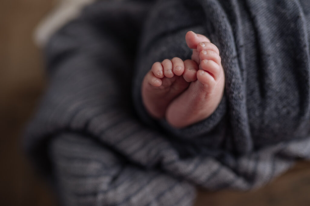 newborn baby toes peek out of a blue blanket