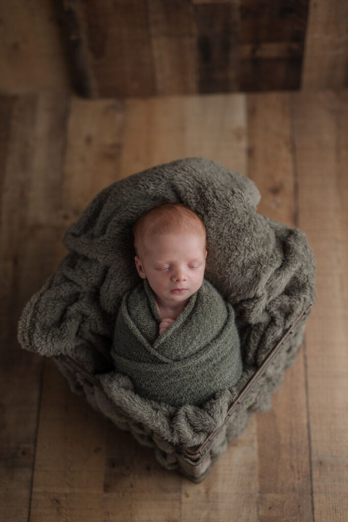 newborn baby boy sleeps while wrapped in greens against a wooden floor backdrop