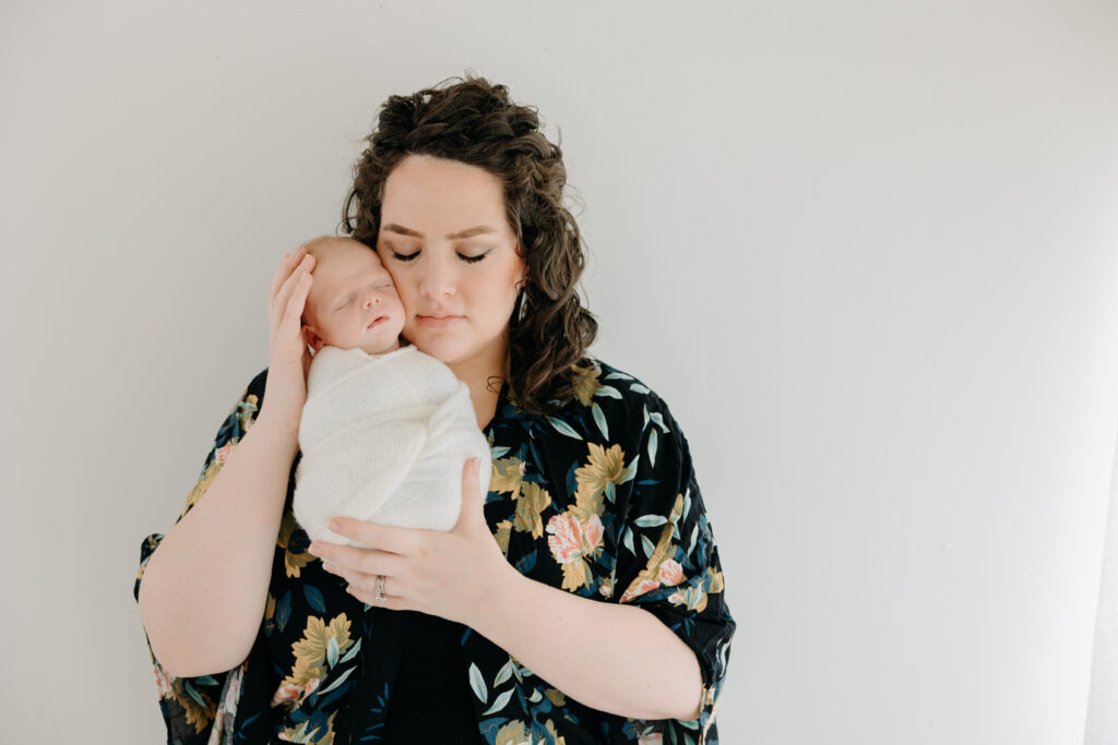 mom snuggles with her newborn baby boy against a white wall