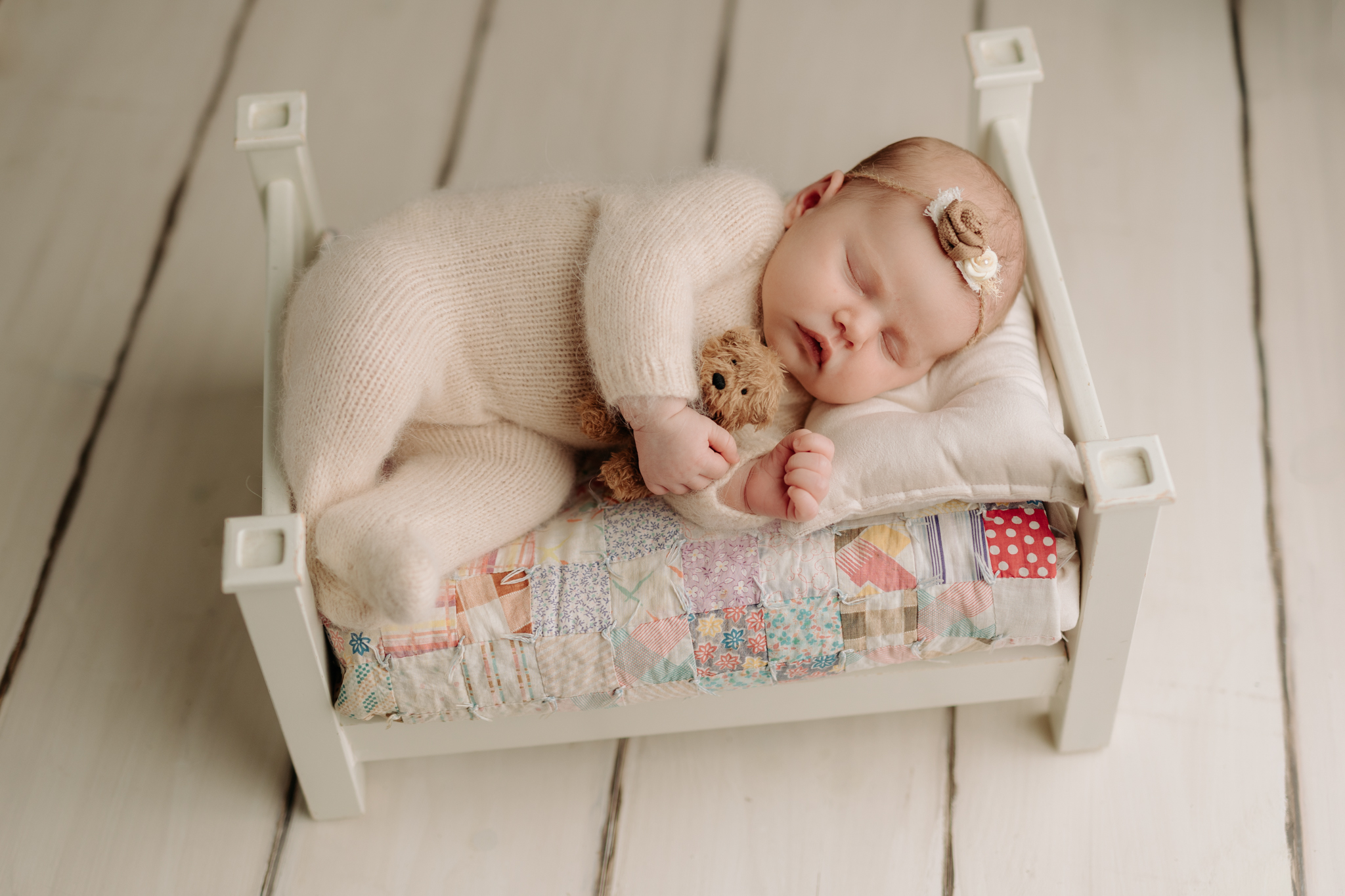 newborn girl lying on white bed with vintage quilt at Pittsburgh newborn photography studio