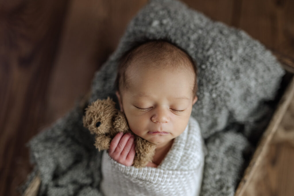 Newborn boy holding a bear at his infant photography session at Kelly Adrienne Photo